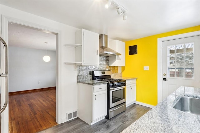 kitchen with white cabinets, backsplash, stainless steel gas range oven, and wall chimney range hood