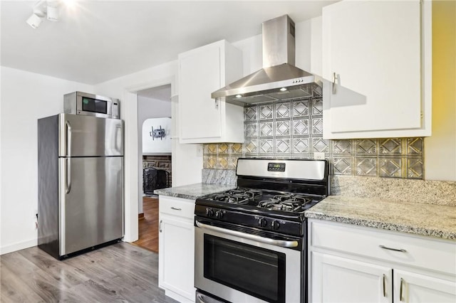 kitchen with white cabinets, wall chimney exhaust hood, decorative backsplash, light stone countertops, and stainless steel appliances