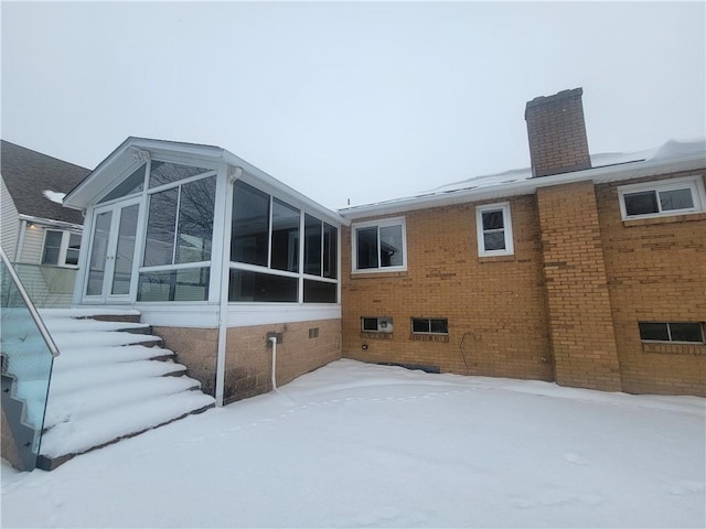 snow covered rear of property with a sunroom