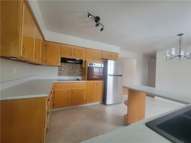 kitchen with tasteful backsplash, stainless steel fridge, oven, track lighting, and decorative light fixtures