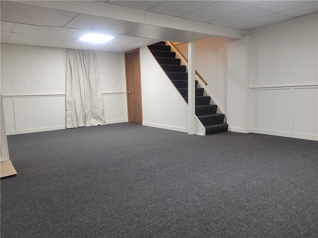 basement featuring a paneled ceiling and dark carpet