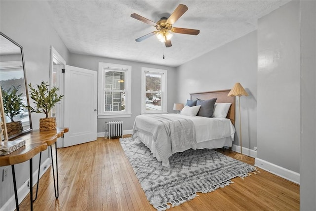 bedroom featuring ceiling fan, light wood-type flooring, radiator heating unit, and a textured ceiling