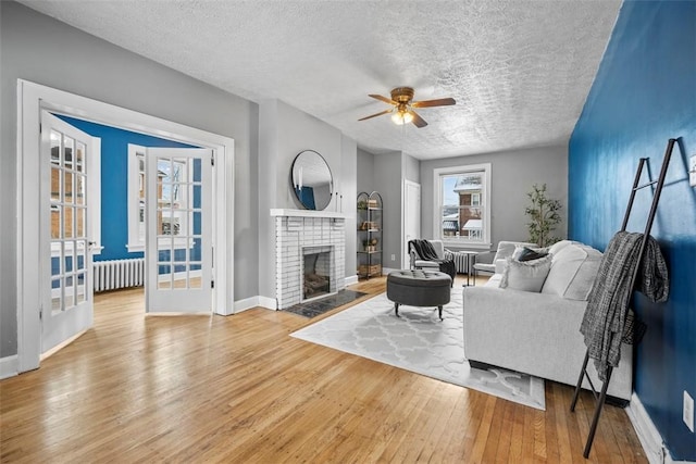 living room with a brick fireplace, ceiling fan, a textured ceiling, light hardwood / wood-style floors, and radiator heating unit