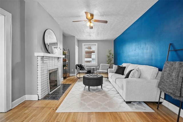 living room featuring a textured ceiling, hardwood / wood-style flooring, a brick fireplace, and ceiling fan