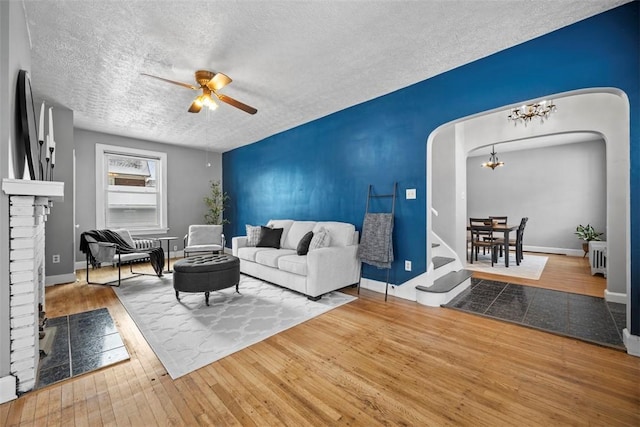 living room featuring ceiling fan with notable chandelier, radiator heating unit, a fireplace, a textured ceiling, and wood-type flooring