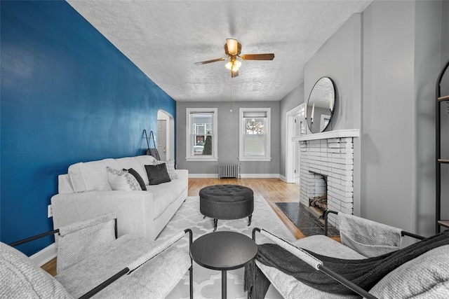 living room featuring radiator, ceiling fan, a textured ceiling, a fireplace, and light wood-type flooring