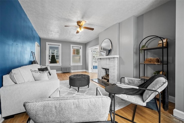 living room with a brick fireplace, radiator, a textured ceiling, ceiling fan, and hardwood / wood-style flooring