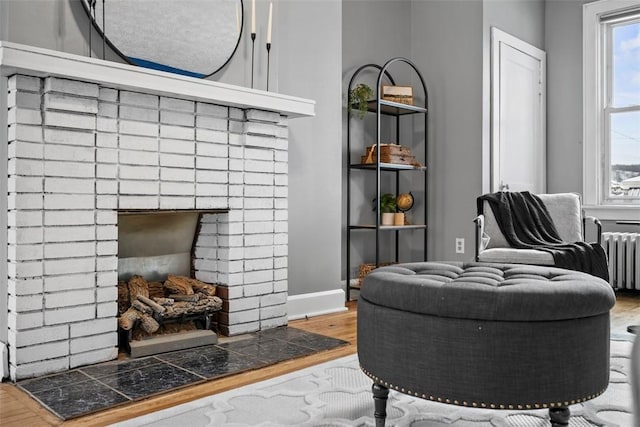 sitting room with radiator heating unit, a brick fireplace, and hardwood / wood-style floors