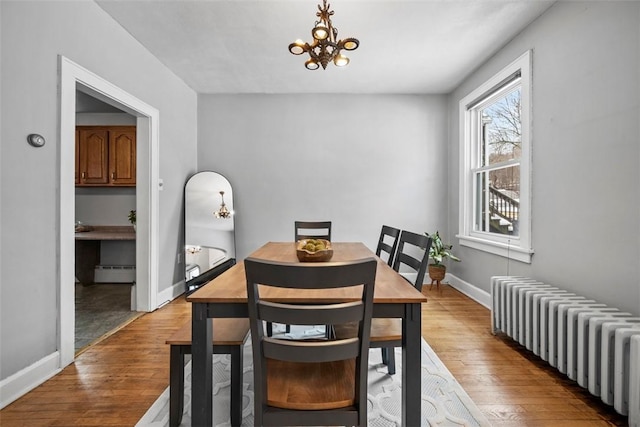 dining area with light wood-type flooring, baseboard heating, radiator, and an inviting chandelier