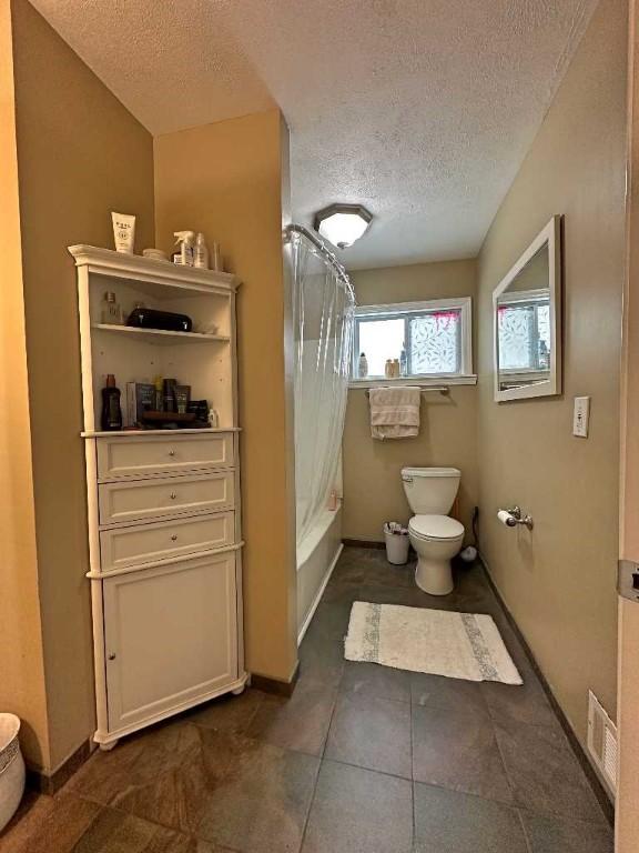 bathroom with a textured ceiling, shower / tub combo, and toilet