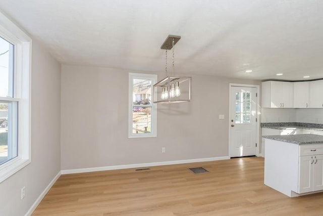 kitchen with a wealth of natural light, white cabinetry, light stone counters, pendant lighting, and light hardwood / wood-style floors