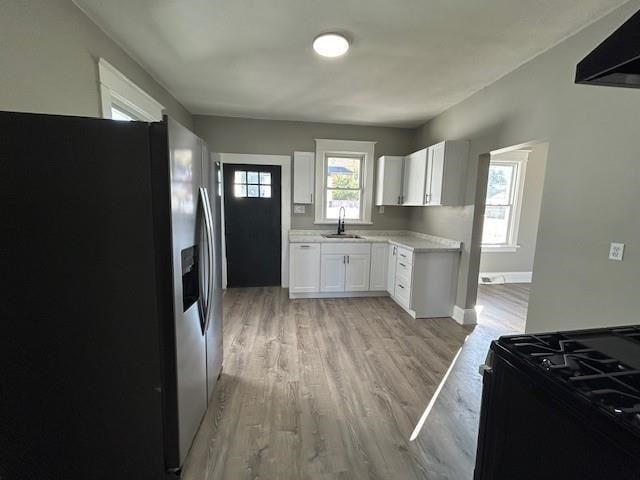 kitchen with black stove, sink, light hardwood / wood-style flooring, stainless steel fridge with ice dispenser, and white cabinetry