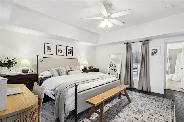 bedroom featuring hardwood / wood-style floors, ceiling fan, ensuite bath, and a tray ceiling