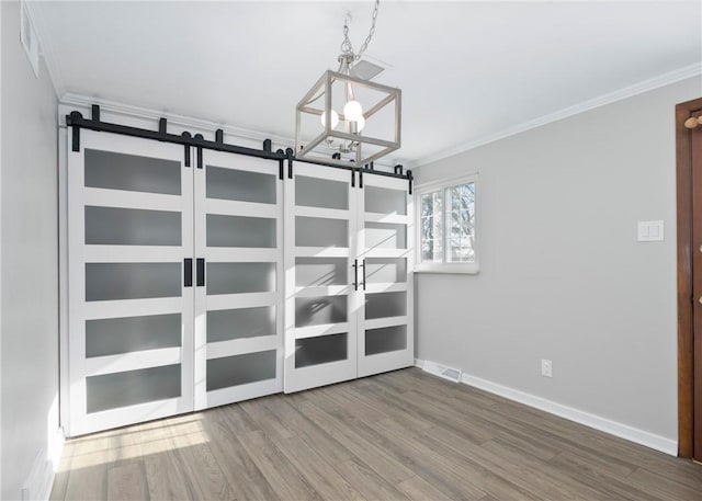 unfurnished room with hardwood / wood-style floors, a barn door, crown molding, and a notable chandelier