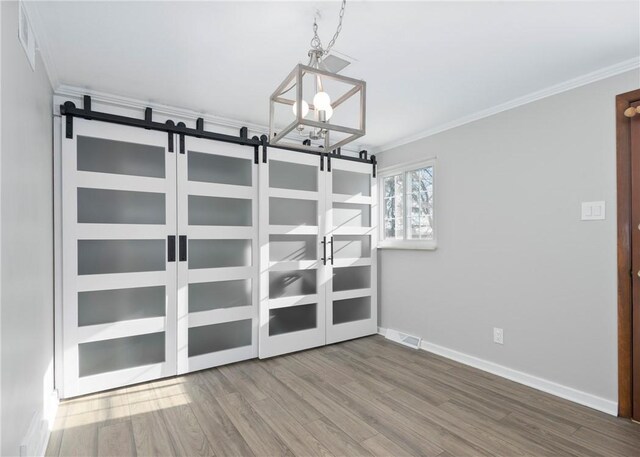unfurnished room with crown molding, a barn door, visible vents, baseboards, and wood finished floors