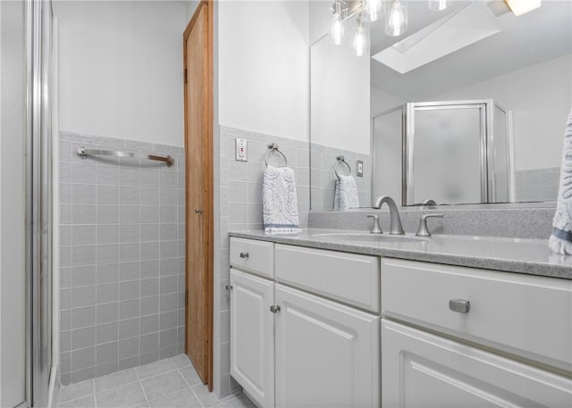 full bath featuring tile walls, a skylight, vanity, a stall shower, and tile patterned flooring