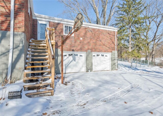 snow covered property with stairway and brick siding