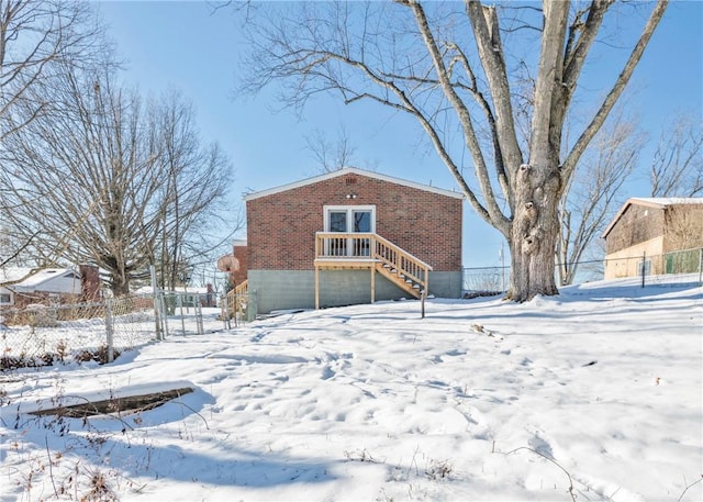 snow covered rear of property featuring fence and brick siding