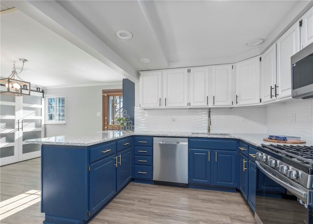 kitchen with a sink, appliances with stainless steel finishes, a peninsula, white cabinetry, and blue cabinets