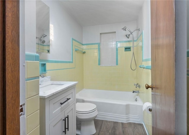 full bathroom with vanity, hardwood / wood-style flooring, tiled shower / bath combo, toilet, and tile walls