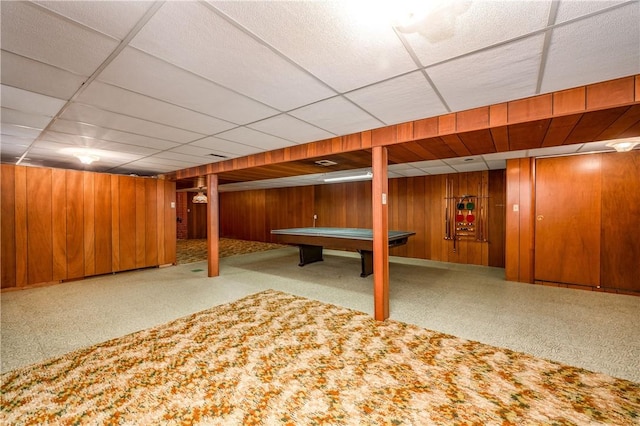 basement with a paneled ceiling, wood walls, and pool table