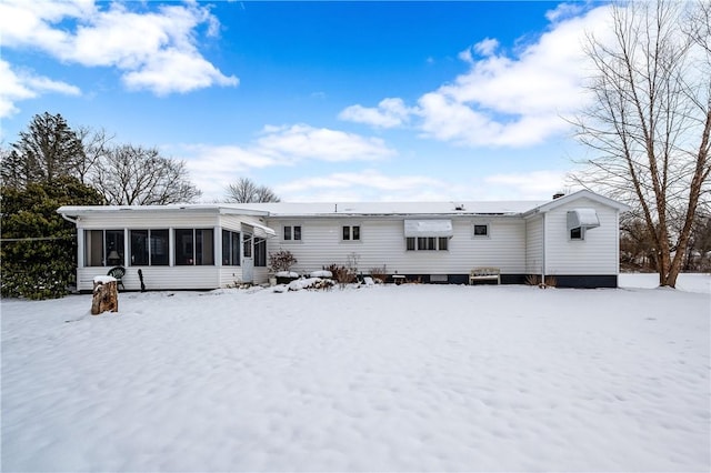 snow covered back of property with a sunroom