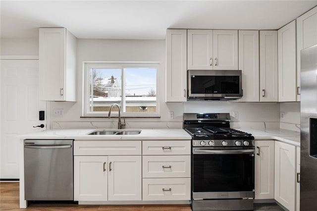 kitchen featuring light stone counters, stainless steel appliances, white cabinetry, and sink