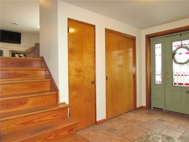 foyer entrance with stairway, baseboards, and stone tile flooring