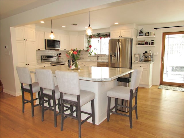 kitchen featuring white cabinetry, stainless steel appliances, decorative light fixtures, a breakfast bar, and a center island