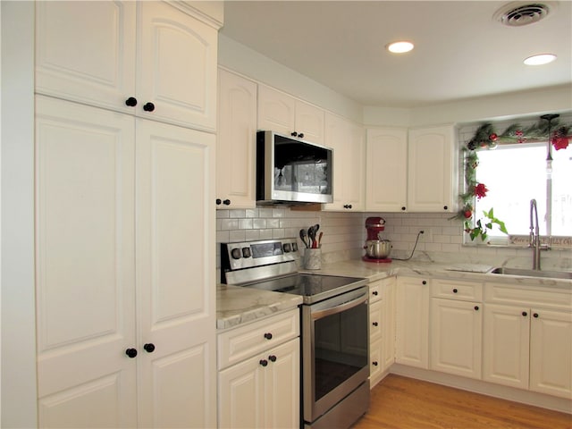 kitchen with appliances with stainless steel finishes, backsplash, white cabinetry, and sink