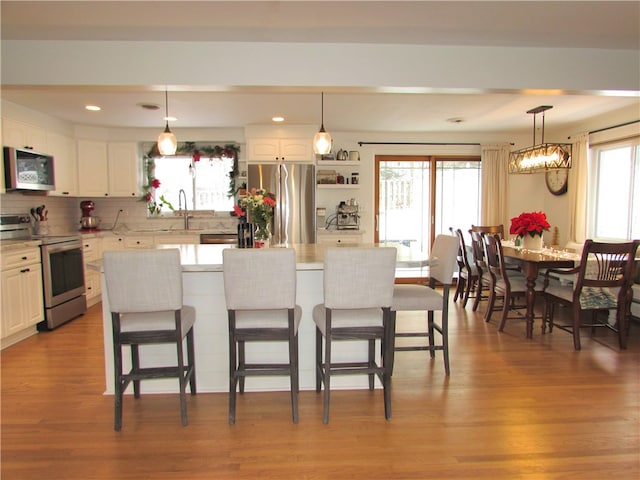 kitchen featuring decorative light fixtures, appliances with stainless steel finishes, white cabinetry, and a center island