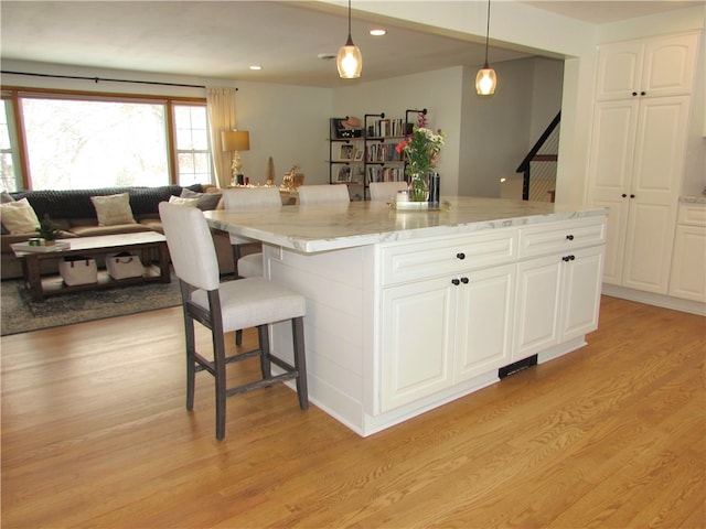 kitchen with light stone countertops, pendant lighting, a center island, white cabinetry, and light hardwood / wood-style flooring