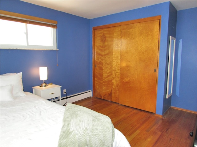 bedroom with a closet, baseboard heating, baseboards, and wood finished floors