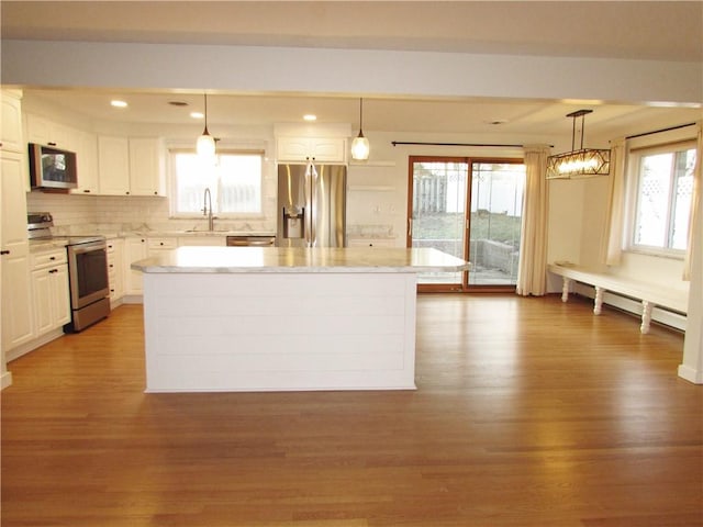 kitchen with a kitchen island, a baseboard heating unit, appliances with stainless steel finishes, white cabinets, and a sink