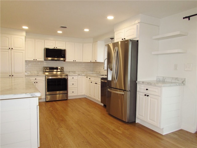 kitchen featuring tasteful backsplash, light stone countertops, light wood-style flooring, appliances with stainless steel finishes, and white cabinets