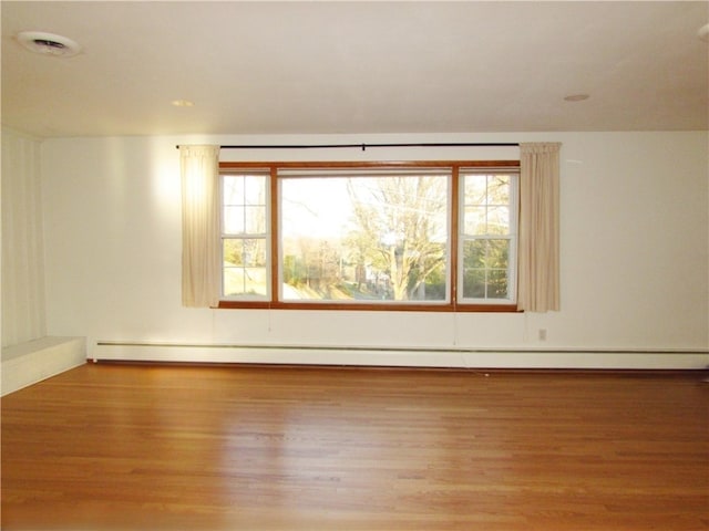 unfurnished room with baseboard heating, visible vents, and wood finished floors