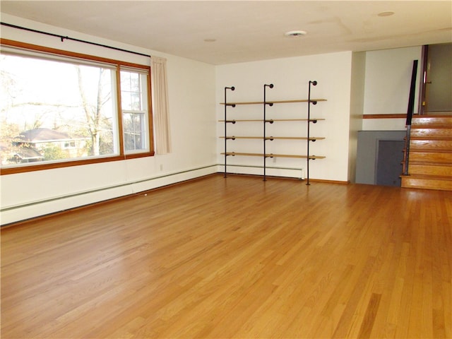 empty room with stairs, wood finished floors, and a baseboard radiator