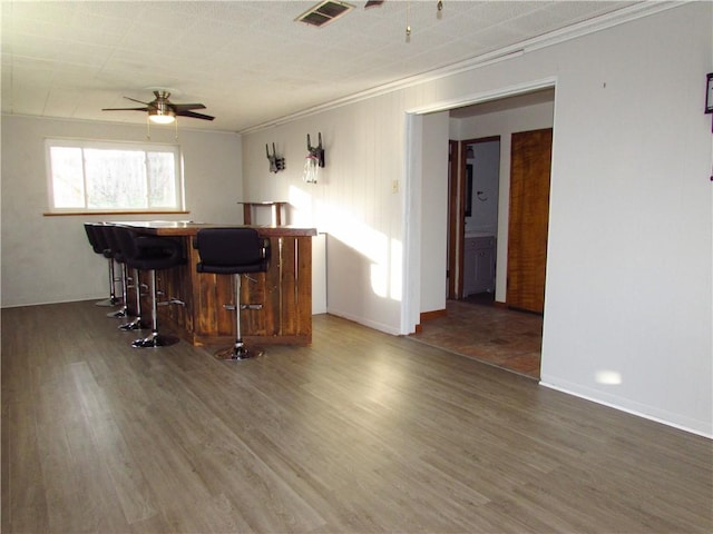 interior space featuring a breakfast bar, wood finished floors, a ceiling fan, and visible vents