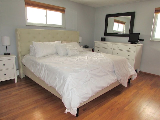 bedroom with multiple windows, wood finished floors, and baseboards