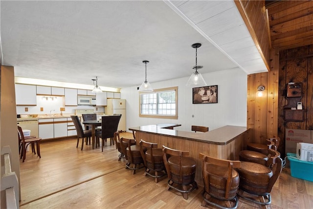 bar featuring white appliances, sink, hanging light fixtures, light wood-type flooring, and white cabinetry