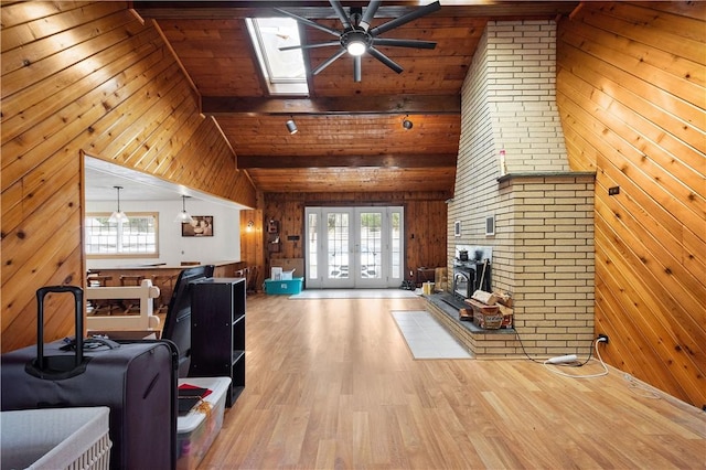 unfurnished living room featuring a skylight, wood walls, high vaulted ceiling, and light wood-type flooring