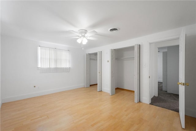 unfurnished bedroom featuring light hardwood / wood-style flooring, ceiling fan, and multiple closets