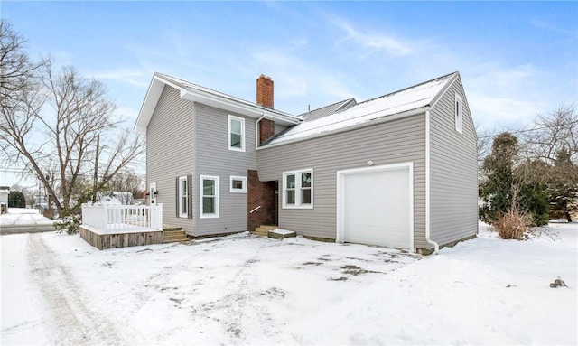 snow covered rear of property with a garage and a wooden deck