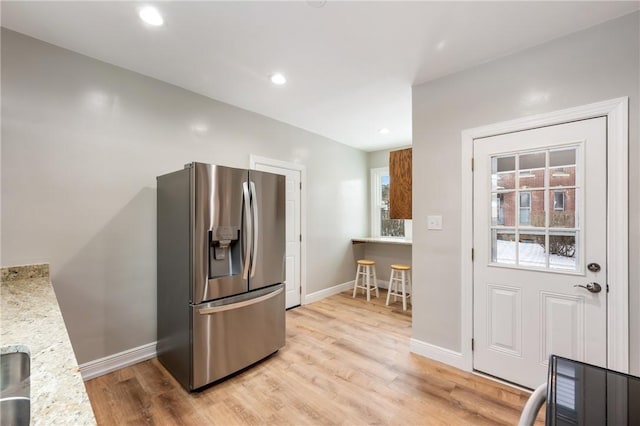 kitchen featuring light stone countertops, stainless steel refrigerator with ice dispenser, and light wood-type flooring