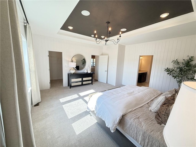 carpeted bedroom with a closet, a walk in closet, ensuite bath, a tray ceiling, and a chandelier