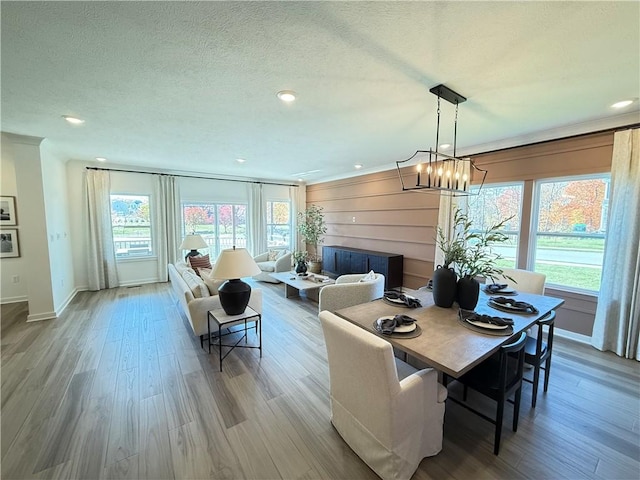 dining space with wooden walls, light hardwood / wood-style floors, a textured ceiling, and a notable chandelier