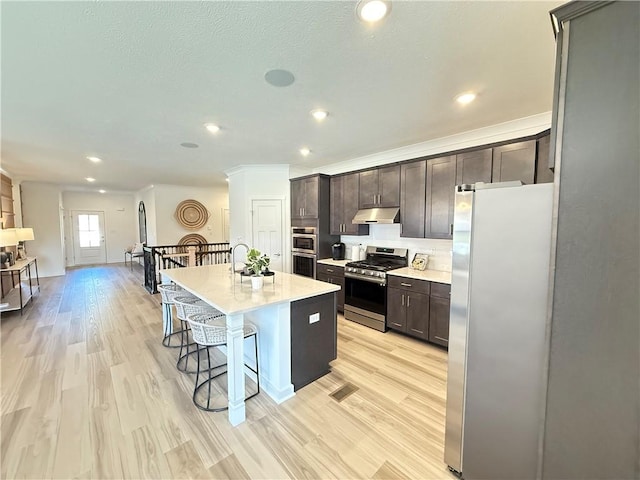 kitchen featuring a center island with sink, a kitchen breakfast bar, light hardwood / wood-style flooring, dark brown cabinetry, and stainless steel appliances