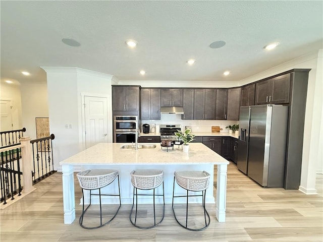 kitchen featuring light stone counters, dark brown cabinetry, a kitchen island with sink, and appliances with stainless steel finishes