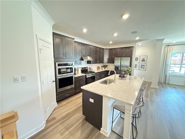 kitchen with a kitchen bar, appliances with stainless steel finishes, light wood-type flooring, a kitchen island with sink, and sink