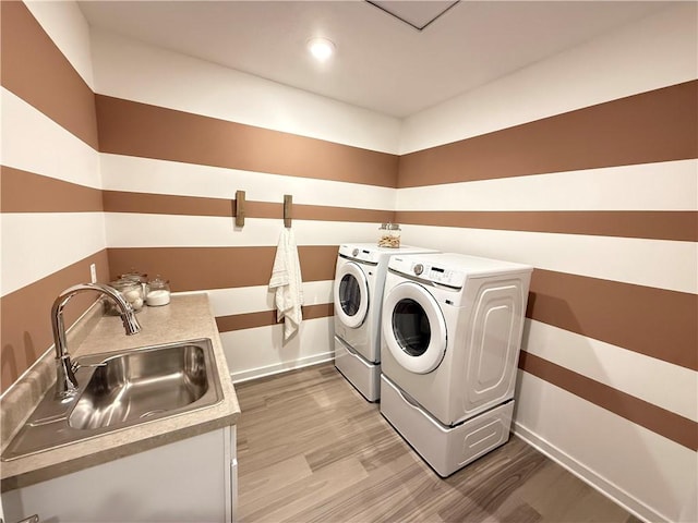 clothes washing area featuring washer and clothes dryer, sink, and hardwood / wood-style floors